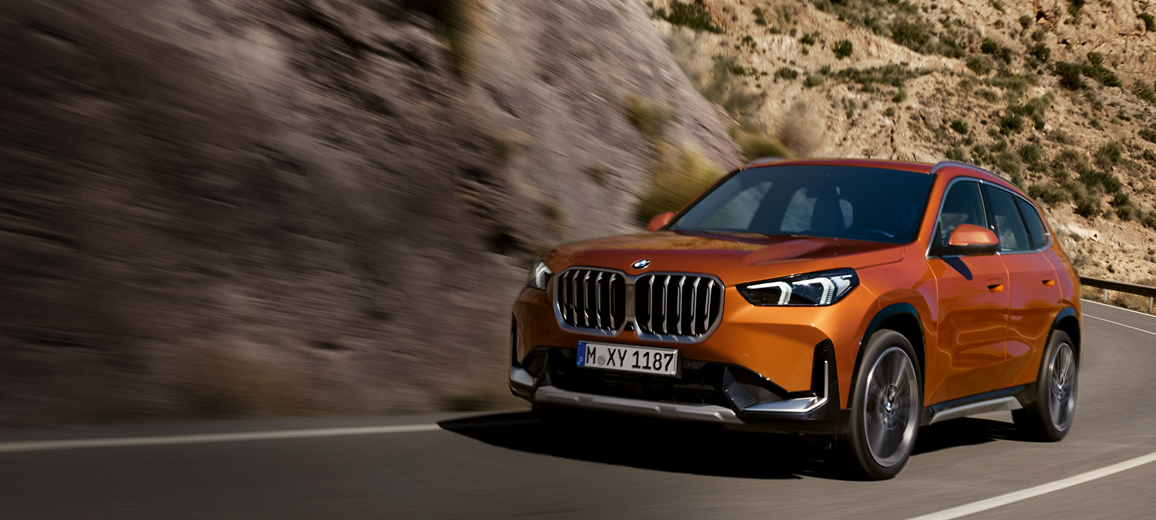 BMW X1 U11 με Έκδοση xLine, πορτοκαλί Utah μεταλλικό, μπροστινή λήψη τριών τετάρτων σε επαρχιακό δρόμο